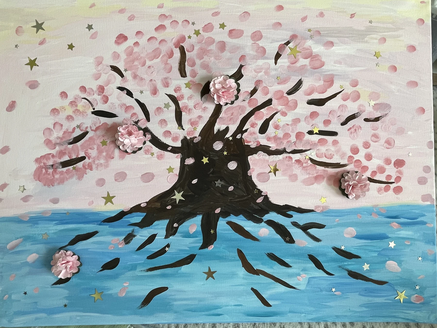 A handmade painting of a flowering pink tree above blue water